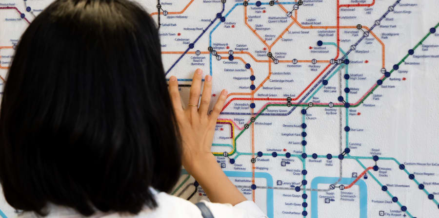 Female student seen from behind with hand reaching up to read braille London Tube map