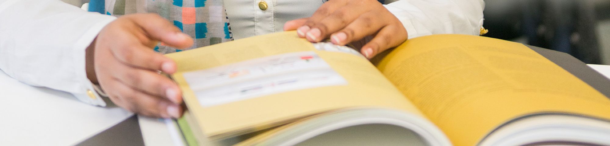 Close up shot of a book on a table and a pair of hands holding it open