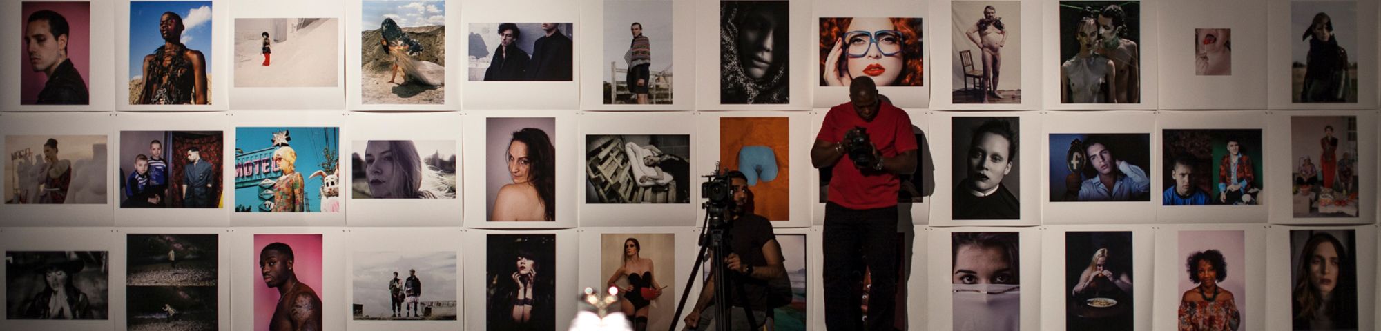 Collage of photos against a white wall with a man standing infron