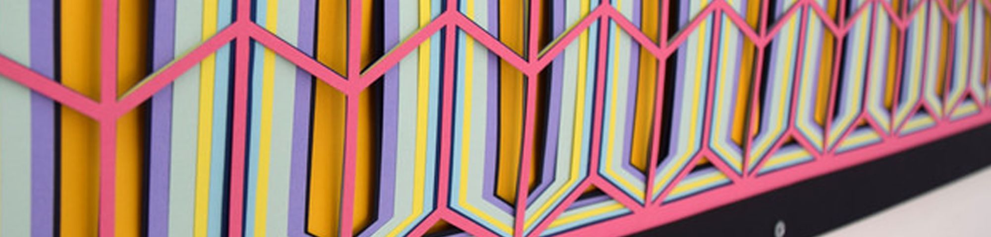 Close up side view of a colourful piece of art in orange, white and pink hanging on a wall