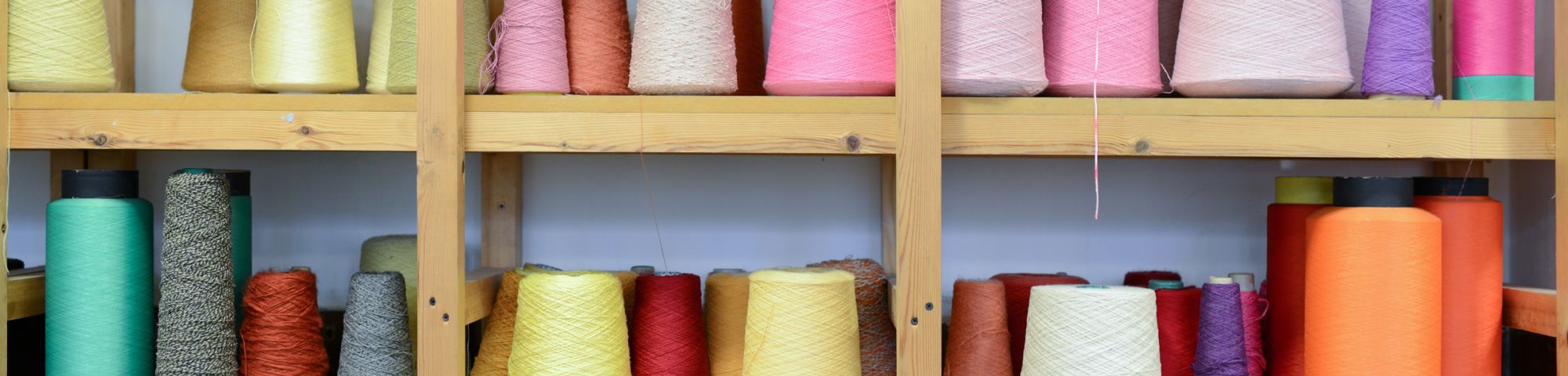 Spools of pink, yellow, blue and orange thread on a shelf