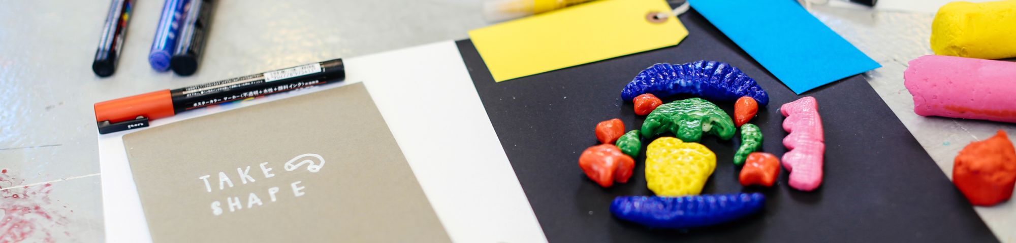 Moulded pieces of colourful clay on a piece of paper with pens and labels next to it