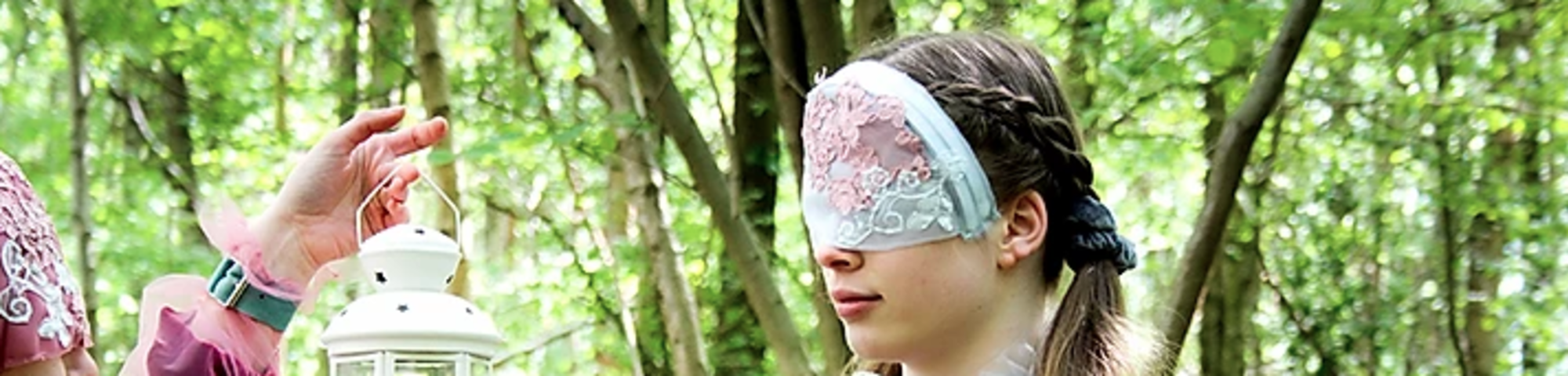 Two masked models interact with eachother while in a forest looking away from the camera wearing garments inspired by the pre-Raphaelite art movement
