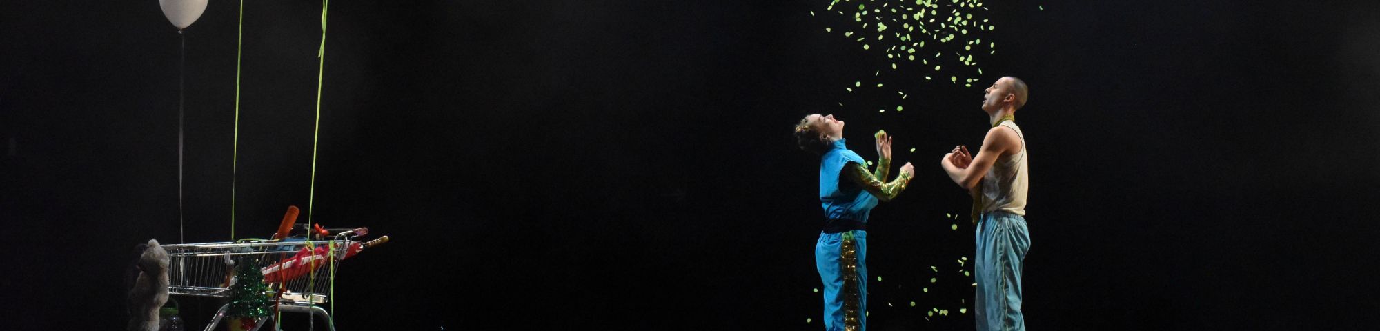 Two performers on stage with green confetti and shopping trolley