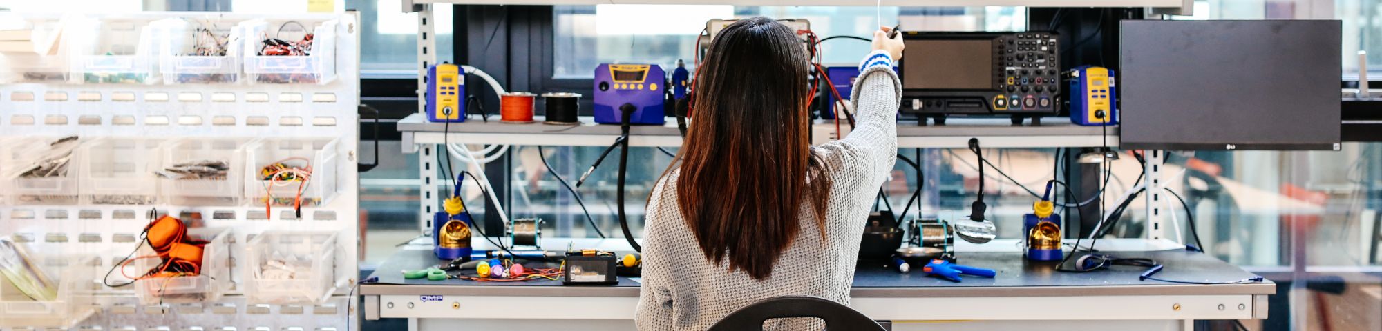 A student working at a desk surrounded by electronic equipment