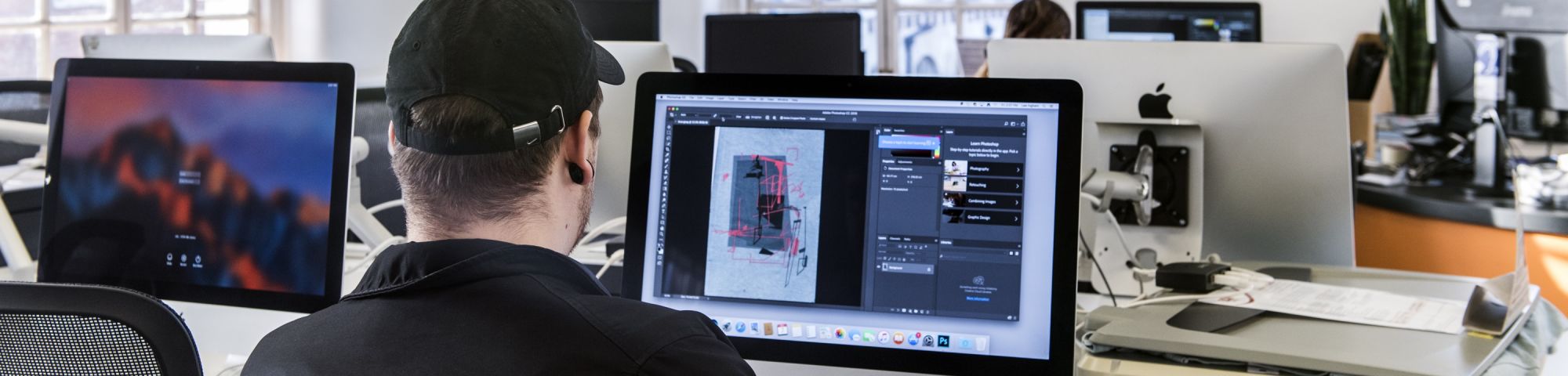 Young man in a cap sitting in front of a computer screen