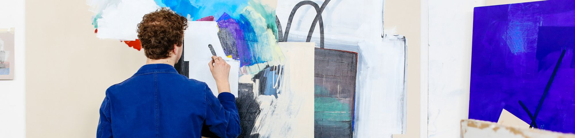 A young man in a blue shirt painting on a canvas