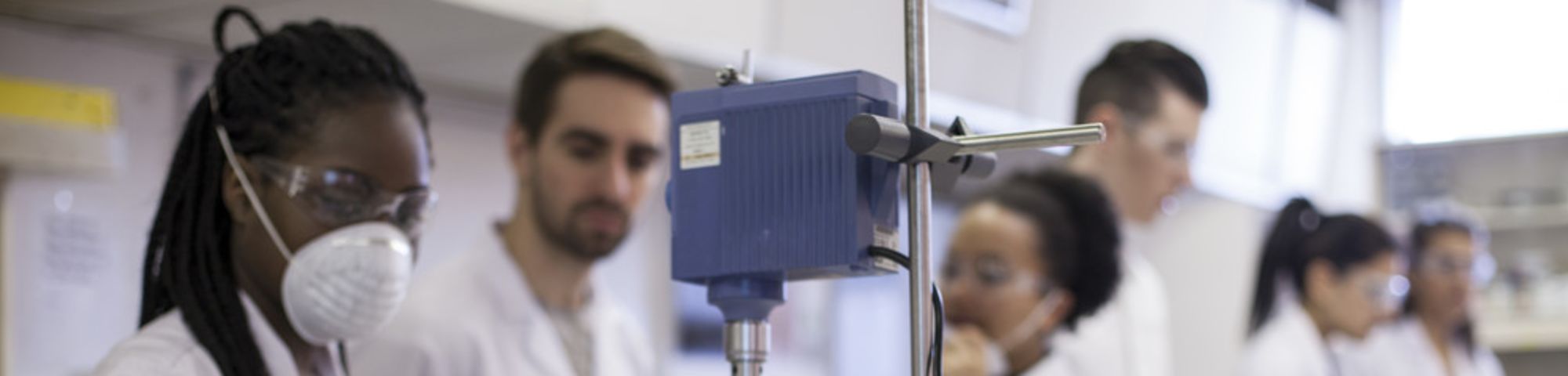 Cosmetic Science students from London College of Fashion in a lab.In the foreground a person is pouring clear liquid into a glass beaker.