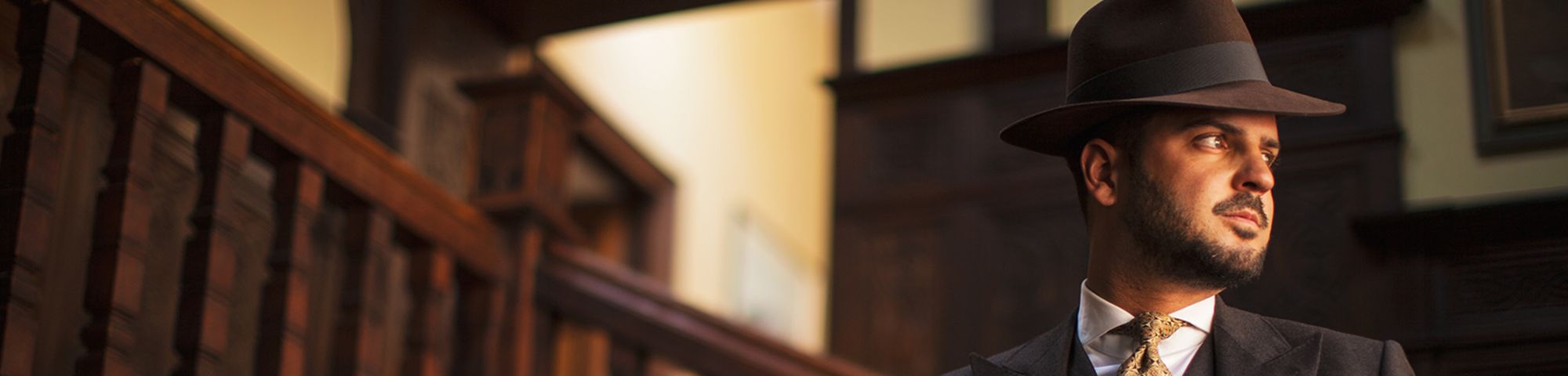 Man wearing tailored suit and hat posing in stairs