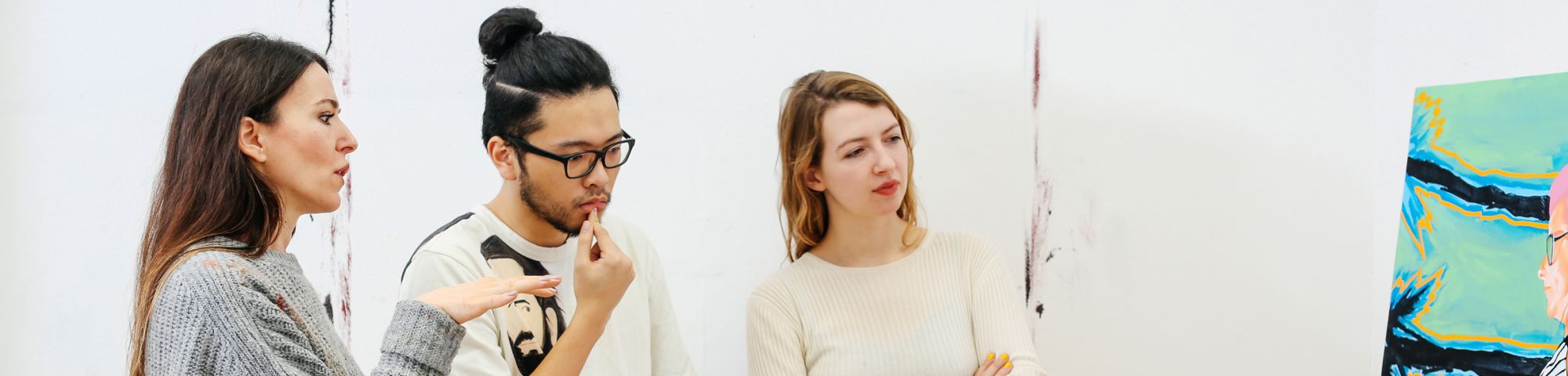 Two women and a man in a studio discussing a painting. One of the women is the artist.