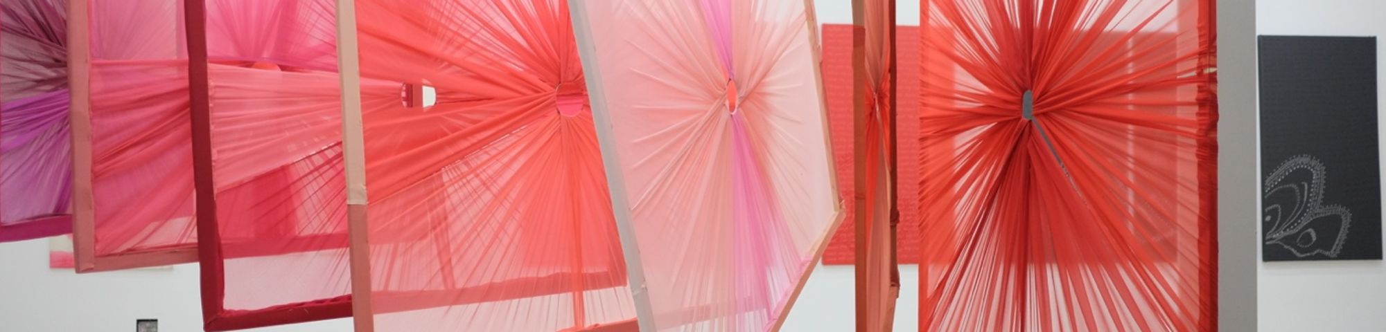 Frames with textile draped around them hanging from the ceiling in a gallery