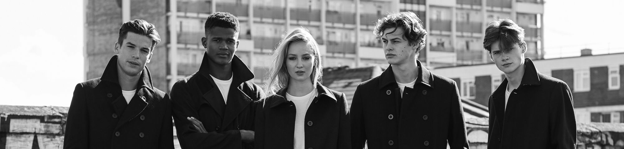 4 male models and 1 female model wearing black and white rustic clothing standing at a block of deserted flats