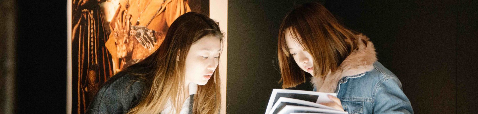 Two female visitors looking at work by media and communication students at MA18 exhibition