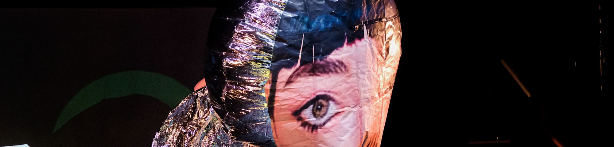 A large helium balloon with a giant eye and section of fringe surrounded by a black backdrop as part of a stage performance.