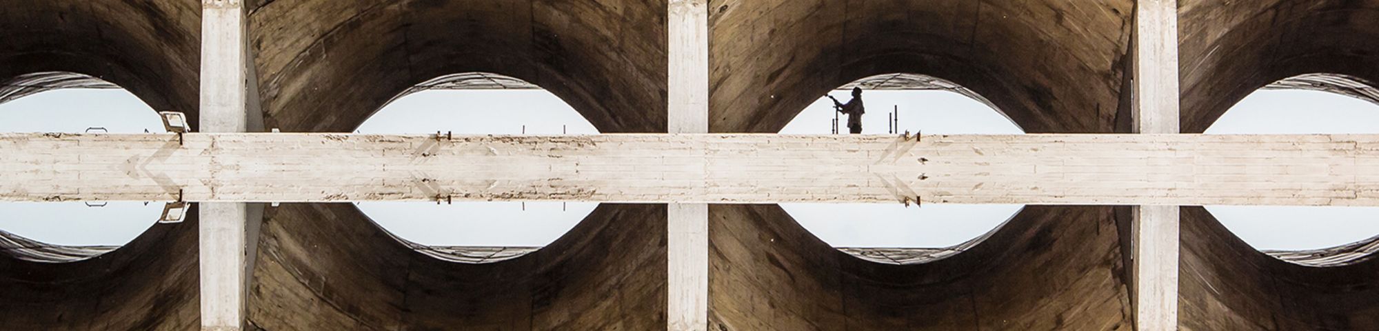 Photograph of the view underneath a concrete bridge, repeated across the image four times and so as to look like the image is reflected.