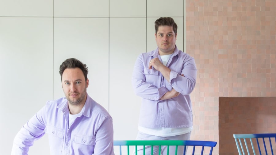 two men in matching lilac outfits sitting on lilac ercol chairs