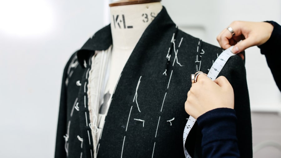 Close up shot of a student taking measurements of a black suit on a mannequin.