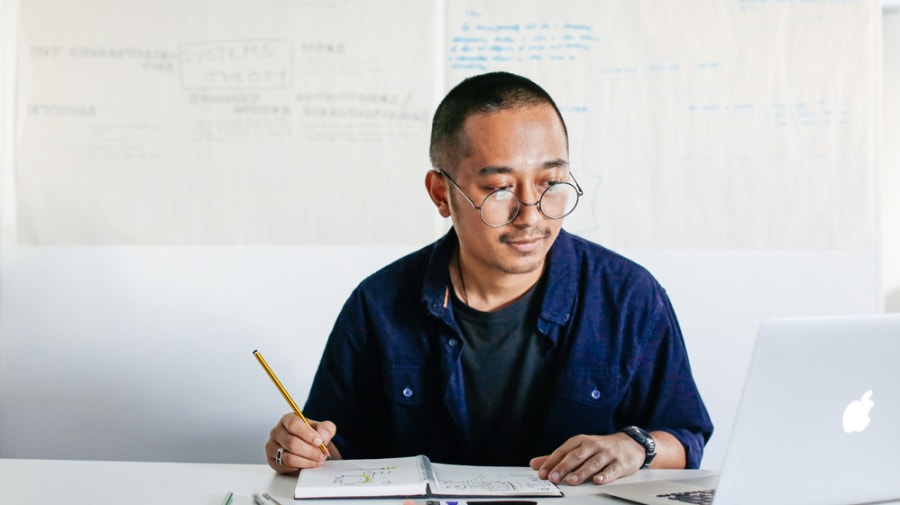 Portrait of student sitting at desk, writing in notebook and smiling.