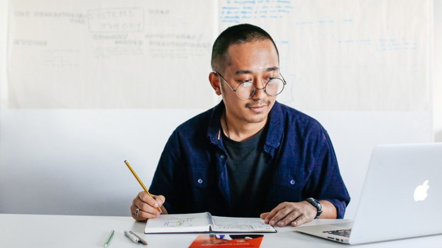 Portrait of student sitting at desk, writing in notebook and smiling.