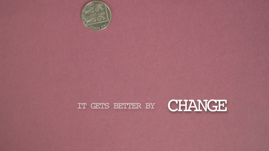 A still of a coin falling in front of a pink background.