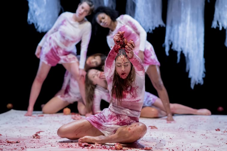 A group of dancers tearing fruit on stage. Their white dresses stained by fruit