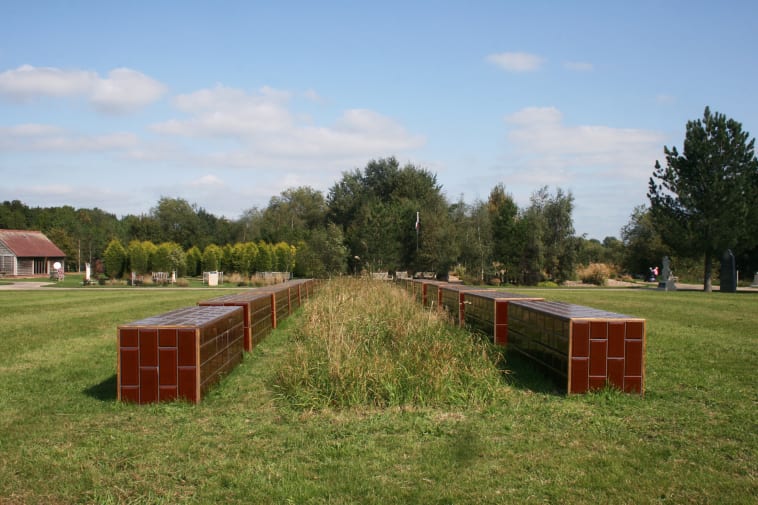 Benches made in brown tiling set in green space with plants and flowers growing in between