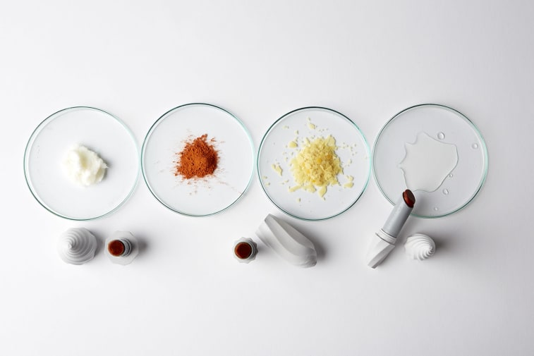 Petri dishes holding coloured powders with lipstick tubes beside