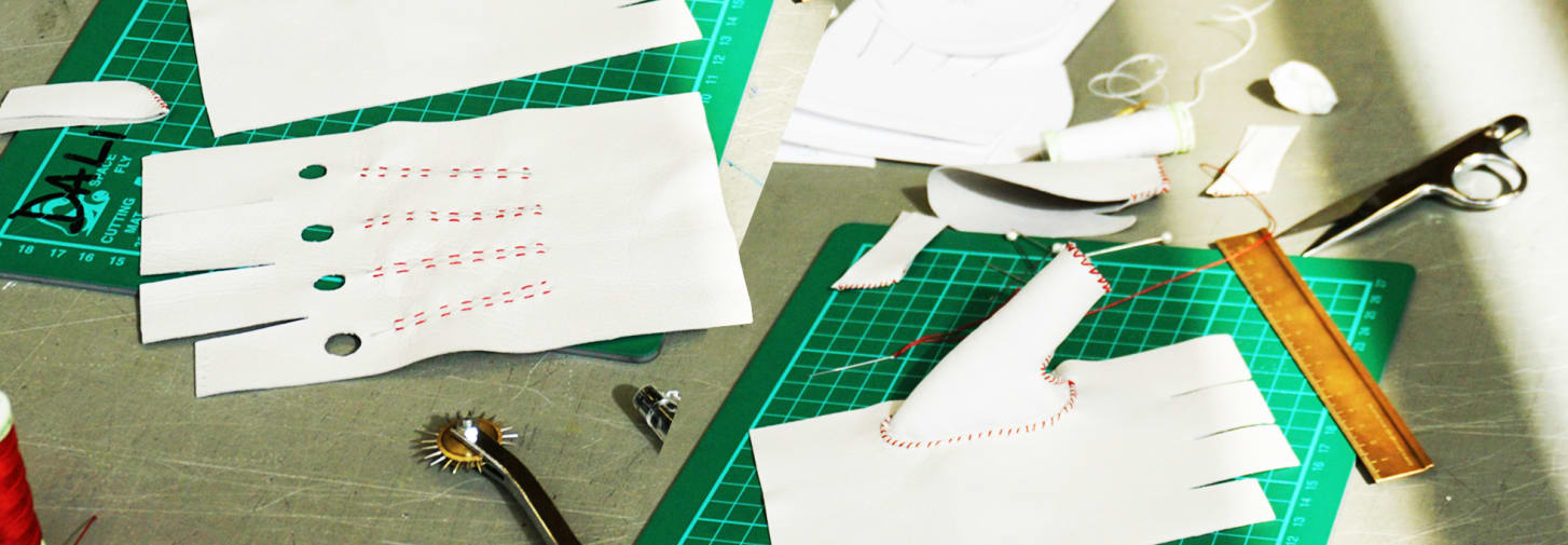 White leather gloves on a desk, being work one, surrounded by material and equipment.