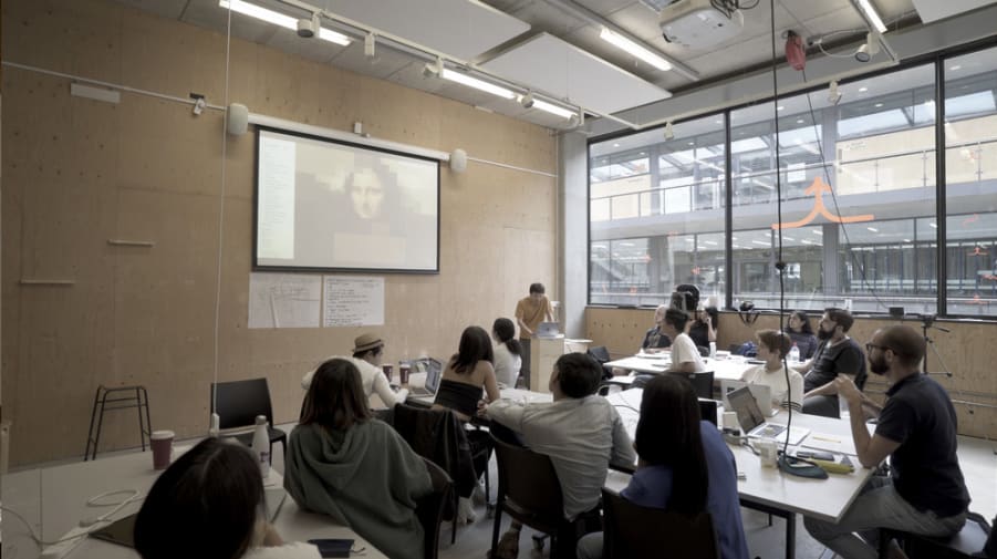 A group of students in a classroom listening to a teacher