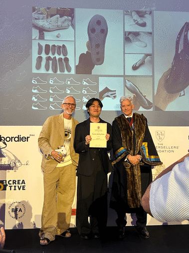 Award winner stood on a stage with two judges and holding a diploma. 