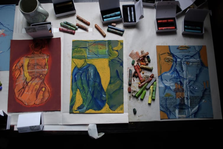 Desk set up showing three pastel drawings on canvas
