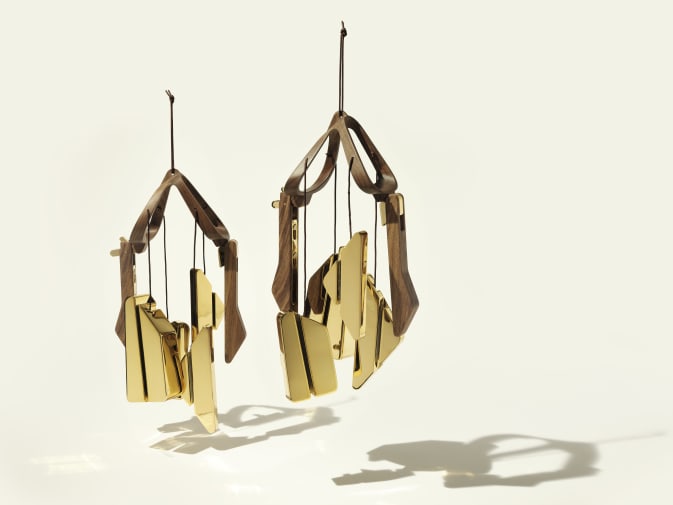 2 windbell shapes floating in the air, they are made from wood and a golden material and casting shadows.