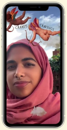 Smiling woman in a salmon coloured headscarf against a blue sky and clouds, with 2 illustrated cherubs above her head and the words 'Cramps' and 'Cravings'