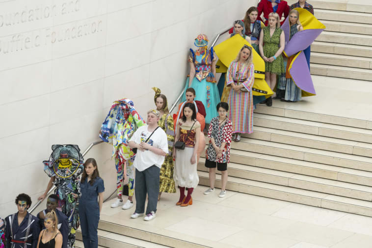 People in colourful costumes lined up on the interior steps of the British Museum, shot from below upwards