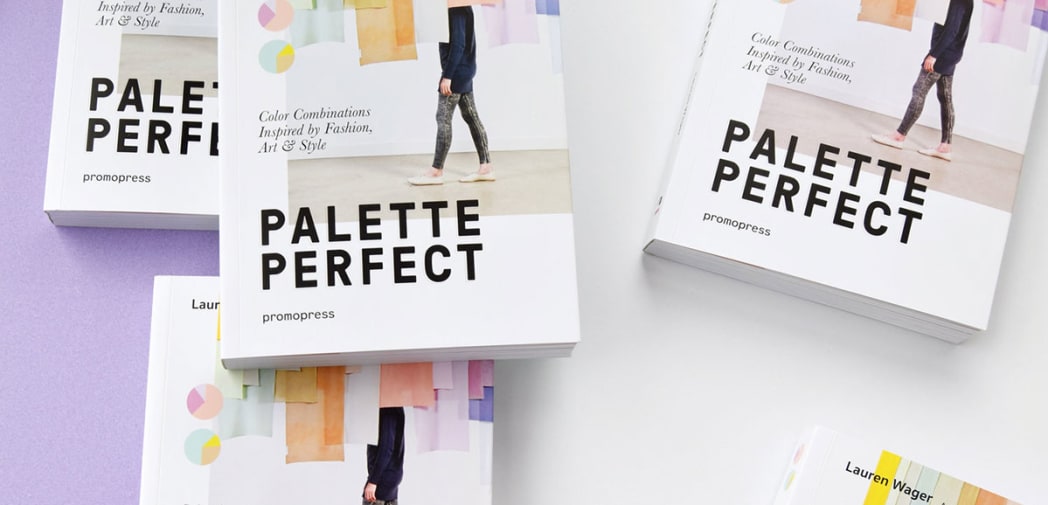 An arrangement of copies of Palette Perfect, the covers of which feature a single figure walking across a gallery space filled with hanging colour banners.