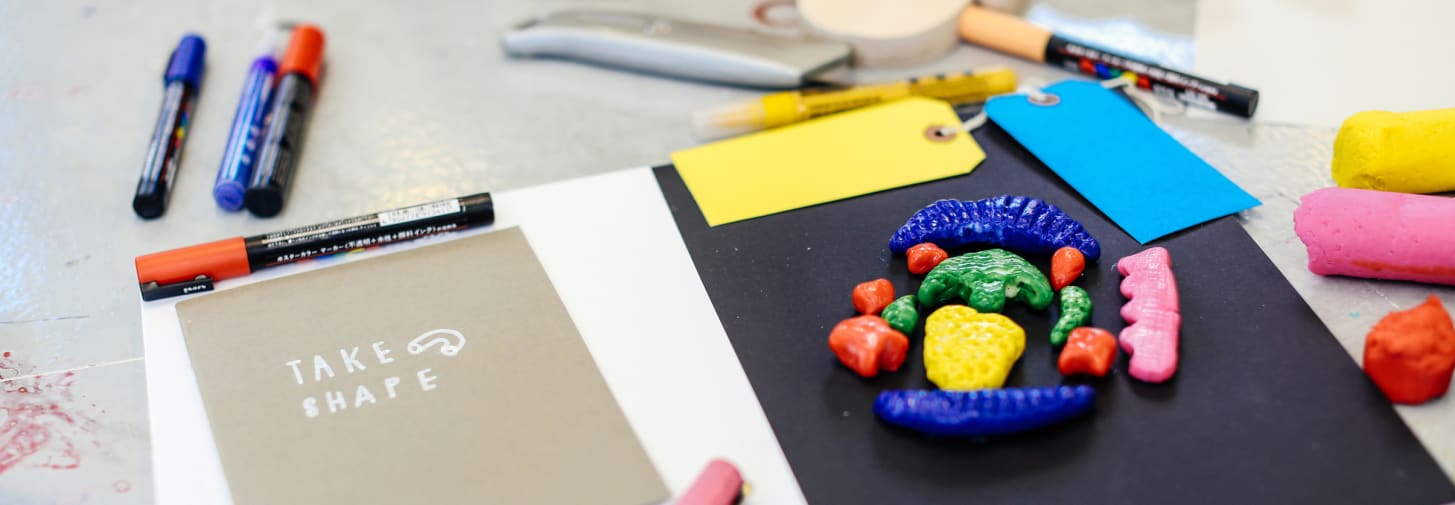 Moulded pieces of colourful clay on a piece of paper with pens and labels next to it