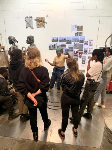 A group of students inside the artist Sokari Douglas Camp's studio which is full of photographs and sculptures