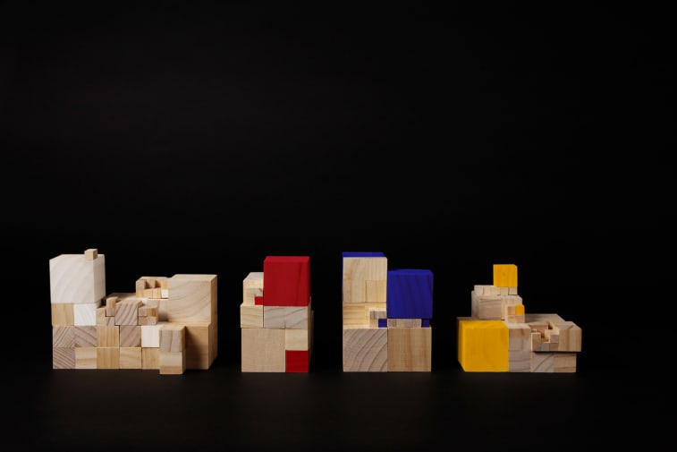 Wooden cube bricks, some coloured in red, yellow and blue, stacked into piles.