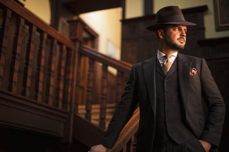 Man wearing tailored suit and hat posing in stairs