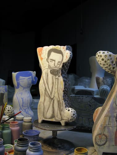 Studio shot of two ceramic vessels with hand drawn illustrations of a man and women