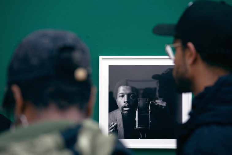 The focus is on a black and white photo of a man in the background, in foreground are 2 guests