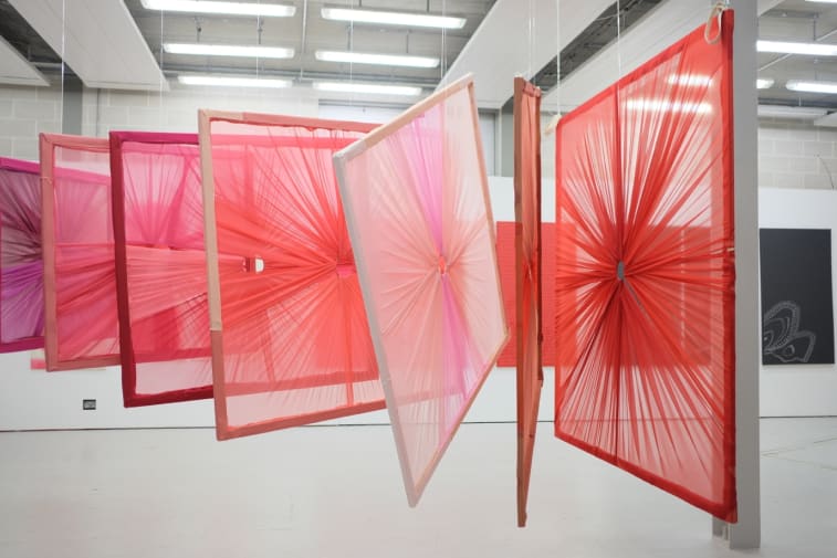 Frames with textile draped around them hanging from the ceiling in a gallery