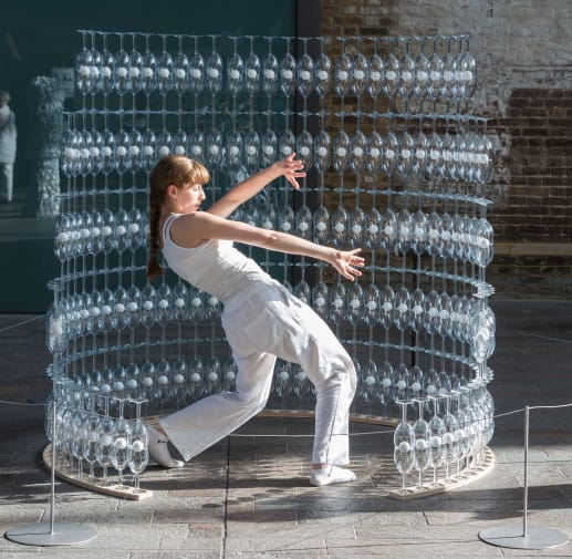 Image of a student doing a dance performance while surrounded by structure constructed from champagne glasses