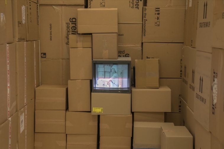 A wall of cardboard boxes with a television sat a centre