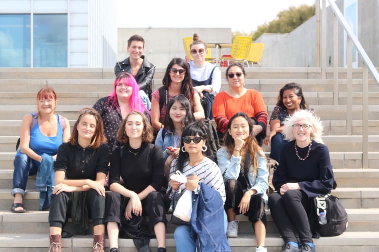 Group Photo of students who came on the annual Post-Grad Community Margate Trip sitting on steps of Turner Contemporary Gallery