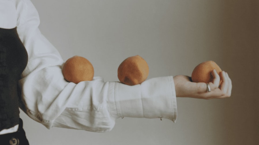 A girl balances three oranges on her arm.