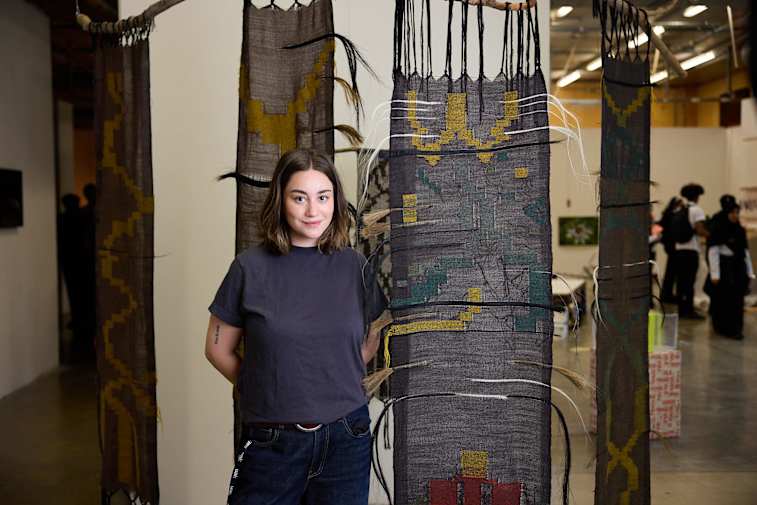 An image of a woman standing in front of a woven tapestry hanging from the ceiling