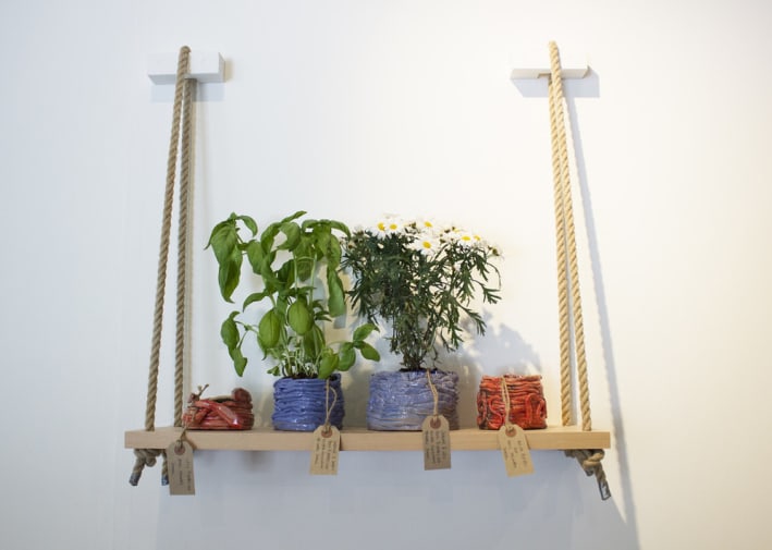 A wooden shelf held up by rope holds 4 colourful plant pots for sale