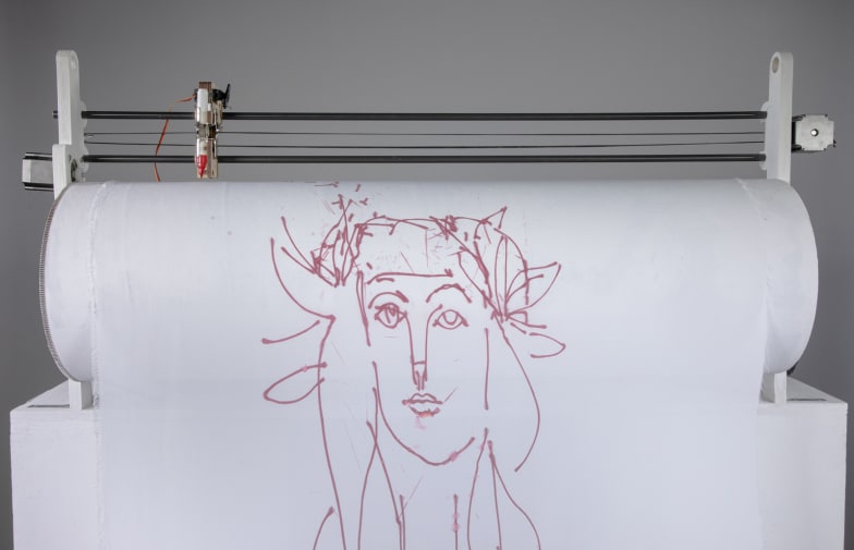 A robot holding sheet of fabric with a drawing of a Picasso-style face, with the sheet of paper on a roller with a pen held
