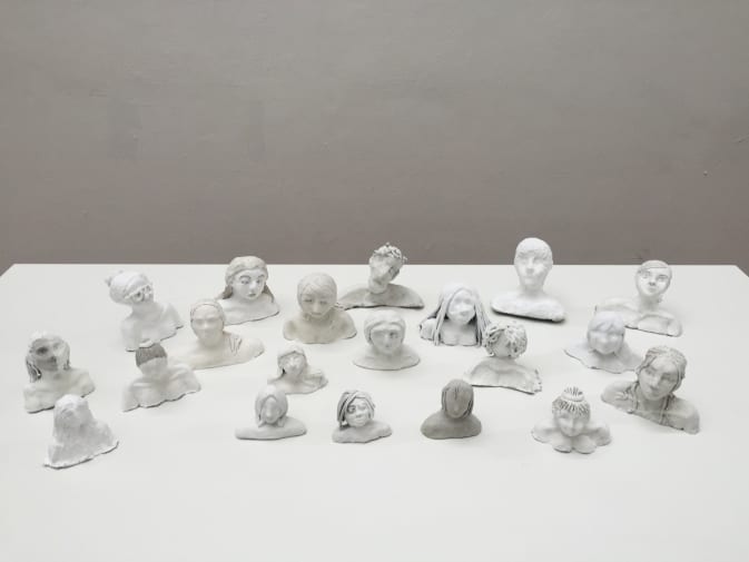 Small head and shoulder sculptures made of clay are arranged on a table